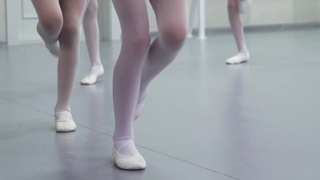 closeup legs of little ballerinas group in white shoes practicing in ballet studio, slow motion. Young girls training elements of classical dance exercise. Childhood, dancing, lifestyle concept