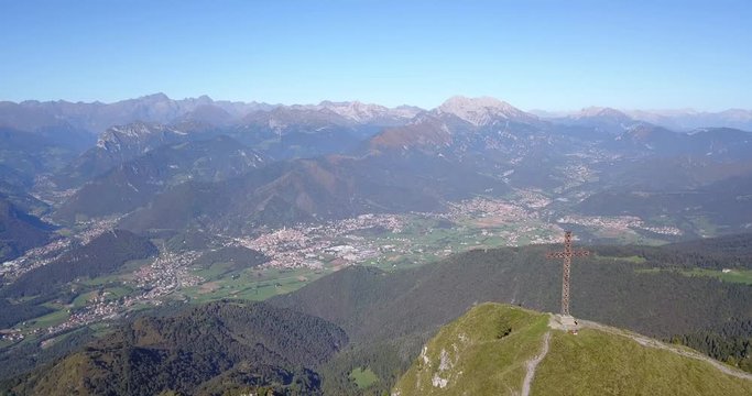 4K Drone aerial view to the Seriana valley and Orobie Alps in a clear and blue day. The cross at the top of the mountain. Landscape from Pizzo Formico Mountain, Bergamo, Italy