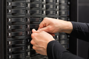 Male IT Engineer Adjusting Hard Drives In SAN At Datacenter