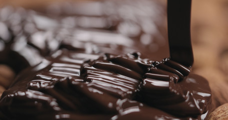 closeup covering roasted almonds with melted dark chocolate