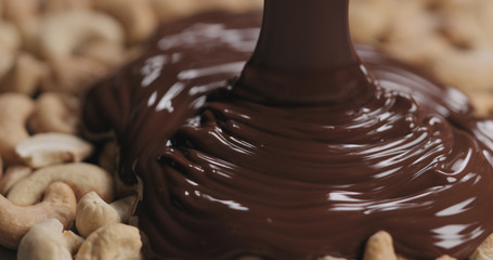 closeup covering roasted cashew with melted dark chocolate