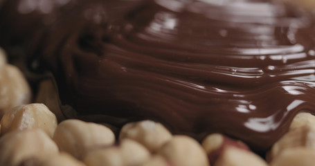 closeup covering roasted hazelnuts with melted dark chocolate