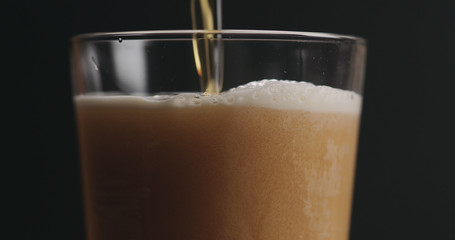 closeup pouring ale beer in a glass over black background