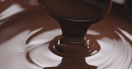 closeup pouring melted dark chocolate from spoon