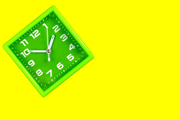 Square green alarm clock on yellow background