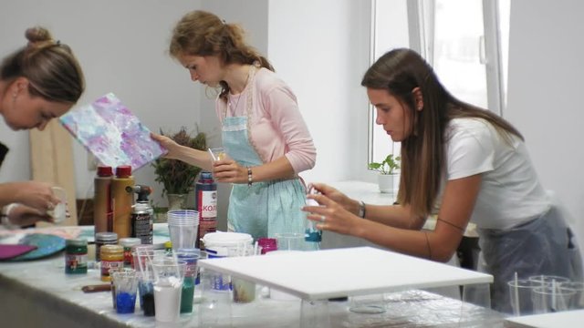 women in an art studio mix paints and draw on canvas in fluid art technique