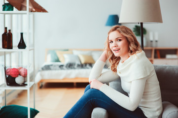 young beautiful woman enjoying time at home, sitting on cozy couch in warm sweater. Happy life, mental health, balance and restore concept