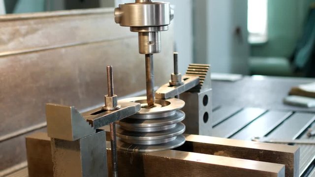 Drilling a hole with a drilling machine in a metal workpiece pulley, close-up, industry, block