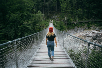 Female blogger or tourist traveller walks on hanging bridge in middle of mountain forest, explores nature in natural surroundings, peace and quiet camping lifestyle, travel destination