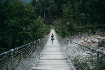 Female blogger or tourist traveller walks on hanging bridge in middle of mountain forest, explores nature in natural surroundings, peace and quiet camping lifestyle, travel destination