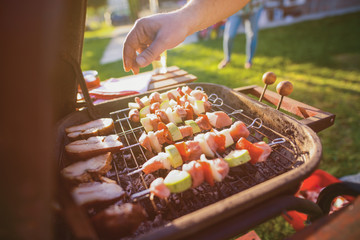 Close up of males hand turning meat and vegetable on barbeque grill.