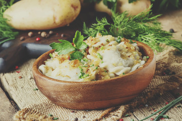 Traditional Russian vareniki with potatoes and fried onions in bowl on old wooden table, rustic style, selective focus