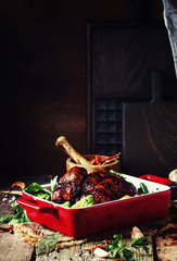 Baked chicken in glaze with vegetables in red form for baking on old wooden table, rustic style, selective focus