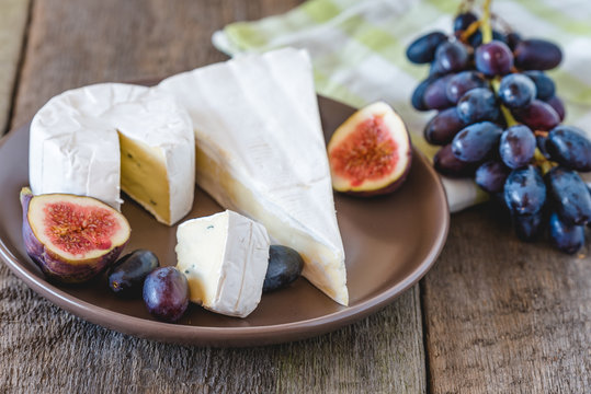 Cheese with fig and grapes on wooden table.