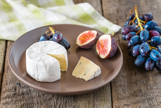 Cheese with fig and grapes on wooden table.