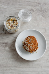 Still life morning breakfast of pancakes with honey and sprinkled with sesame seeds and muesli in glass on a white plate on a wooden background.