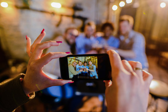 Close up of females hands taking a picture of four happy male friends drinking in a bar.