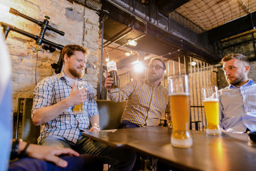 Close up of glass full of beer. Tree male friends sitting in a bar and drinking beer.