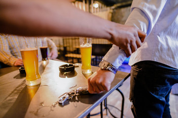 Close up of males hand holding hand of his friend in a bar and stopping him to drive a car after drinking alcohol.