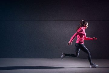 Fototapeta na wymiar Sporty strong sporty woman running against black wall.