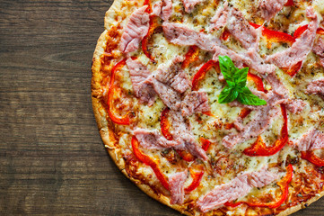 Pizza with Mozzarella cheese, ham, pepper, meat, Tomatoes, Spices and Fresh Basil. Italian pizza on wooden background