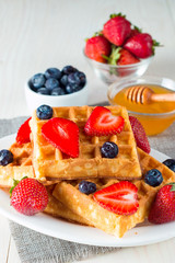 Photo of fresh homemade food made of berry Belgian waffles with honey, chocolate, strawberry, blueberry, maple syrup and cream. Healthy dessert breakfast concept with juice. 