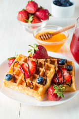 Photo of fresh homemade food made of berry Belgian waffles with honey, chocolate, strawberry, blueberry, maple syrup and cream. Healthy dessert breakfast concept with juice. 