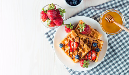 Photo of fresh homemade food made of berry Belgian waffles with honey, chocolate, strawberry, blueberry, maple syrup and cream. Healthy dessert breakfast concept with juice. 