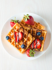 Photo of fresh homemade food made of berry Belgian waffles with honey, chocolate, strawberry, blueberry, maple syrup and cream. Healthy dessert breakfast concept with juice. 