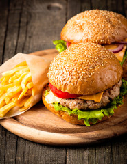 Close-up photo of home made hamburger with beer made of beef, onion, tomato, lettuce, cheese and spices. Fresh burger closeup on wooden rustic table with potato fries and chips.