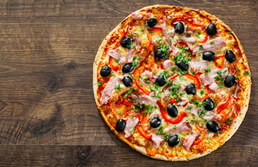 Pizza with Mozzarella cheese, ham, pepper, meat, Tomatoes, olives, Spices and Fresh Basil. Italian pizza on wooden background