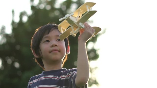 Cute Asian child playing wooden airplane in the park outdoors slow motion 