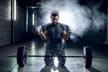 Picture of strong sporty bodybuilder preparing him self for heavy lifting. Kneeling in front of...