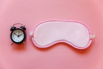 Sleeping eye mask, alarm clock isolated on pink pastel colourful trendy background. Do not disturb me, let me sleep. Rest, good night, siesta, insomnia, relaxation, tired, travel concept