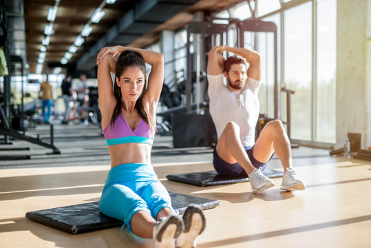 Picture of fit handsome sporty couple sitting in a bright gym and stretching their arm muscles after training.