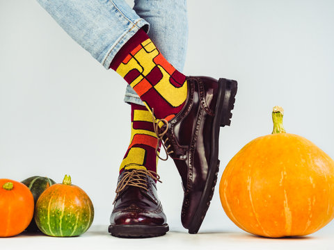 Beautiful pumpkins, gifts tied with a red ribbon, men's legs in stylish, vintage shoes and bright, multi-colored socks. White background, isolated, close-up. Holidays, fashion, elegance