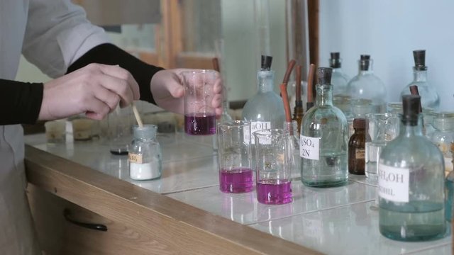 Woman scientist carrying out laboratory research in retro old style research lab. Chemical reaction changing color in vintage chemistry laboratory.
