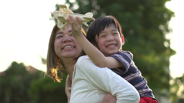Cute Asian mother and son playing wooden airplane together in the park outdoors slow motion 