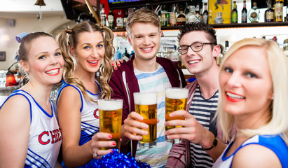 Fans of a sports team watching game in bar drinking beer