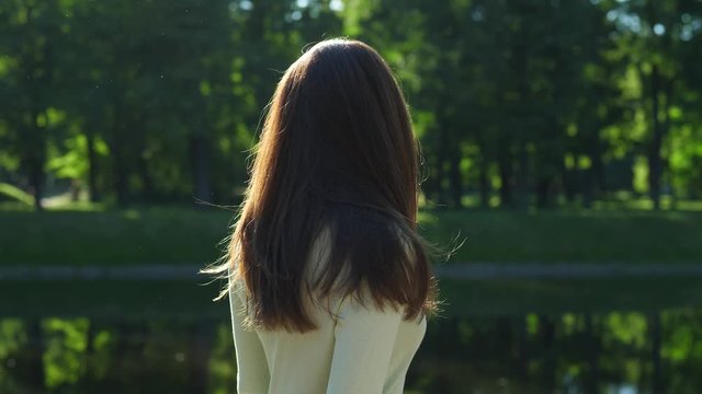 Woman flip her long shiny hair against green foliage