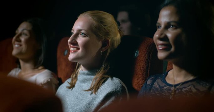 Happy young woman sitting in a movie theatre smiling and enjoying a great moment in the movie.