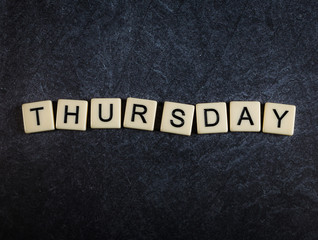 Fototapeta premium Scrabble letter tiles on black slate background spelling Thursday