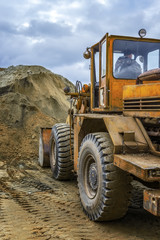 Bulldozer on construction site. Rear view. against the background of rain clouds. Pile of sand in front of the tractor
