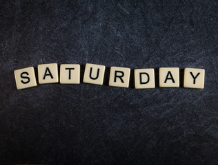 Scrabble letter tiles on black slate background spelling Saturday