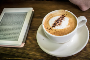 cup of coffee and e-reader on wooden table