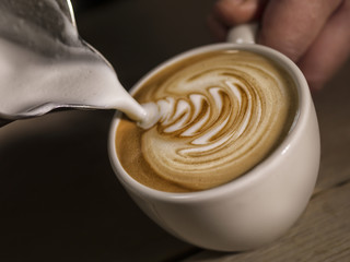 Close up hand of barista making cappuccino coffee pouring milk making latte art