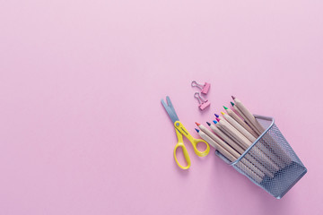 Top view over a pink background with school supplies on it. Coloured pencils, paper clips and scissors as back to school concept. Office supplies flat lay.