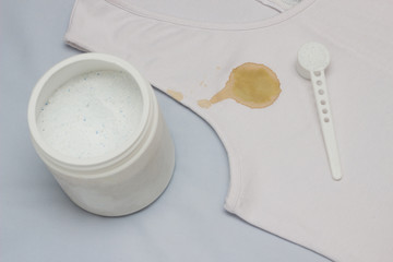 A spot on a white T-shirt, next to it is a container with a stain remover, close-up, bleach