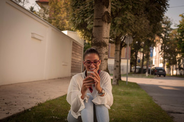 Young woman with smart phone laughing on the street .