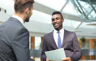 Two multinational young businessmen discussing business at meeting in office.